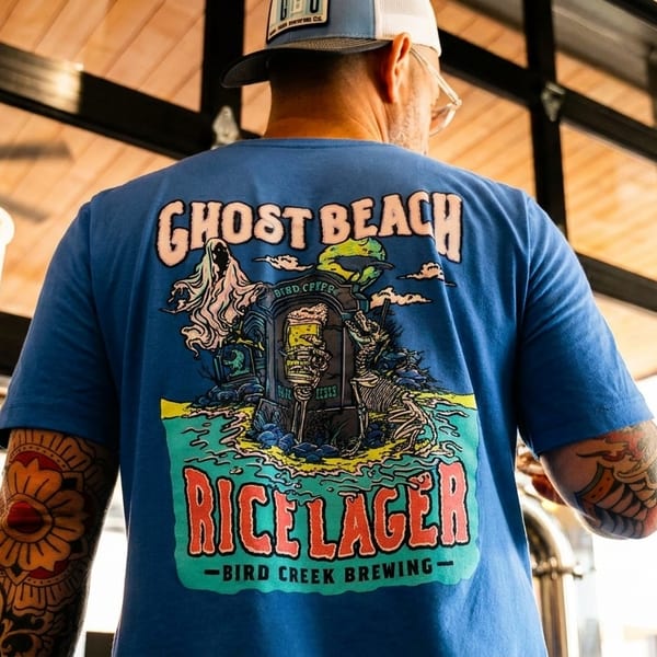 A person wearing a blue "Ghost Beach Rice Lager" t-shirt with a spooky design, facing away from the camera.
