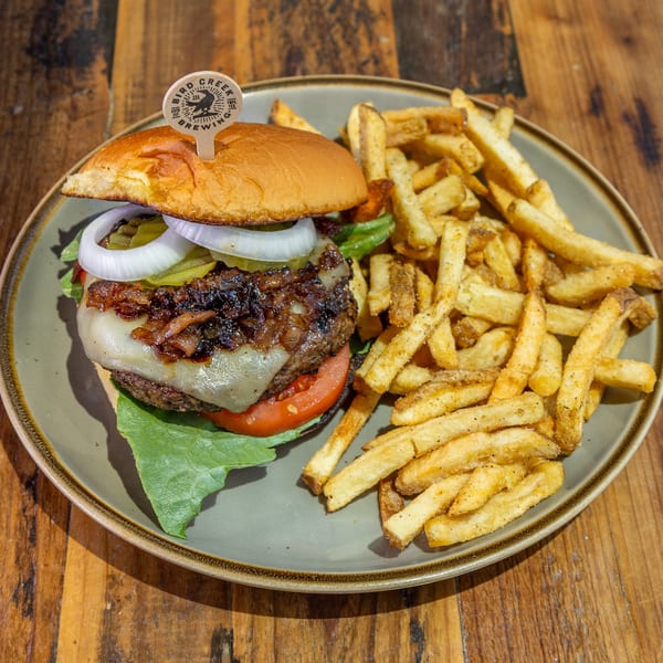 A burger with caramelized onions, cheese, lettuce, tomato, and onion, served with fries on a plate.