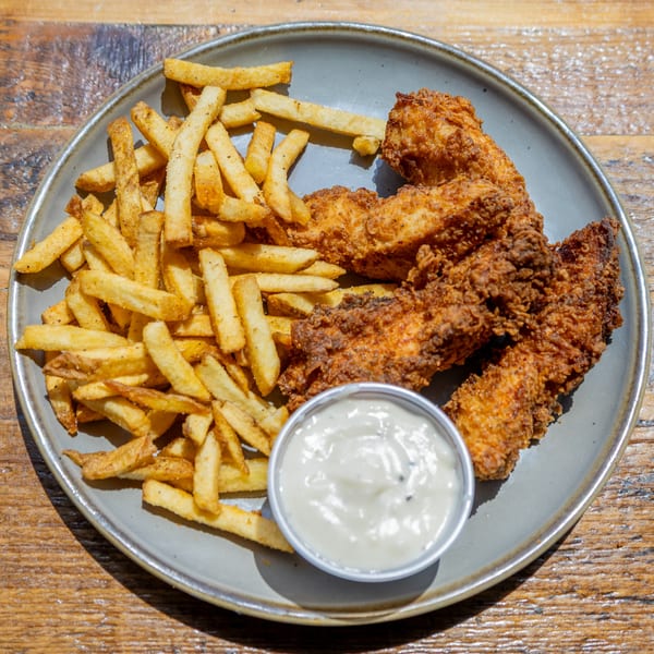 Crispy fried chicken tenders and golden french fries with a side of dipping sauce on a gray plate.