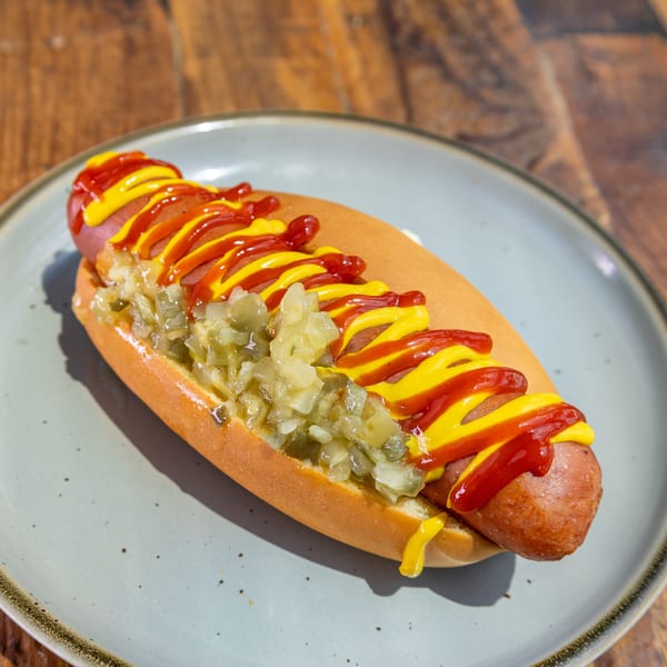Hot dog in a bun with relish, ketchup, and mustard on a light blue plate.