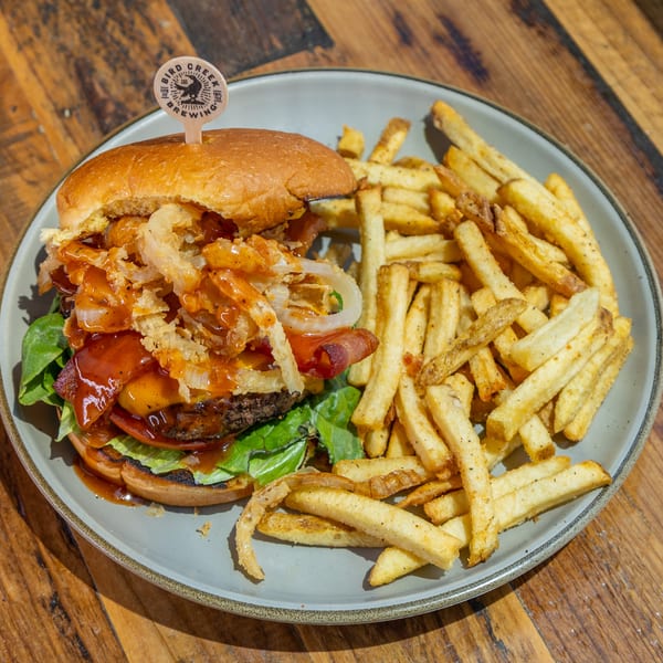 A burger with bacon, cheese, onion rings, and BBQ sauce, served with french fries on a plate.