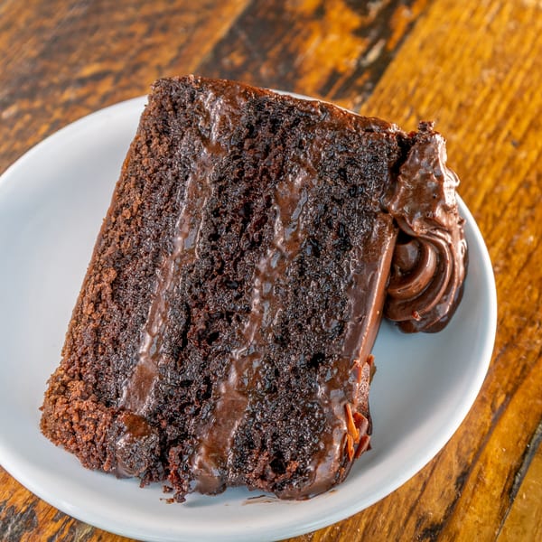 A rich slice of chocolate cake with chocolate frosting and a dollop of whipped chocolate cream.