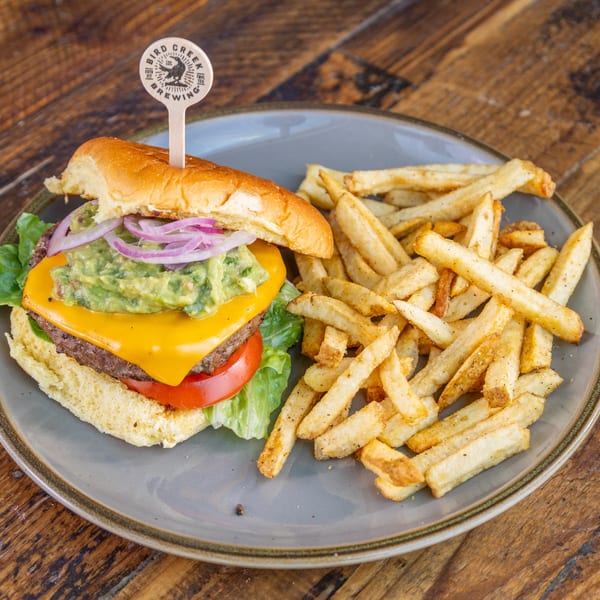 A Bird Creek Brewing burger with guacamole, cheese, and red onion, served with fries on a gray plate.